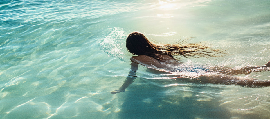 Seamlessly blended hair extensions on a woman swimming in clear ocean water.
